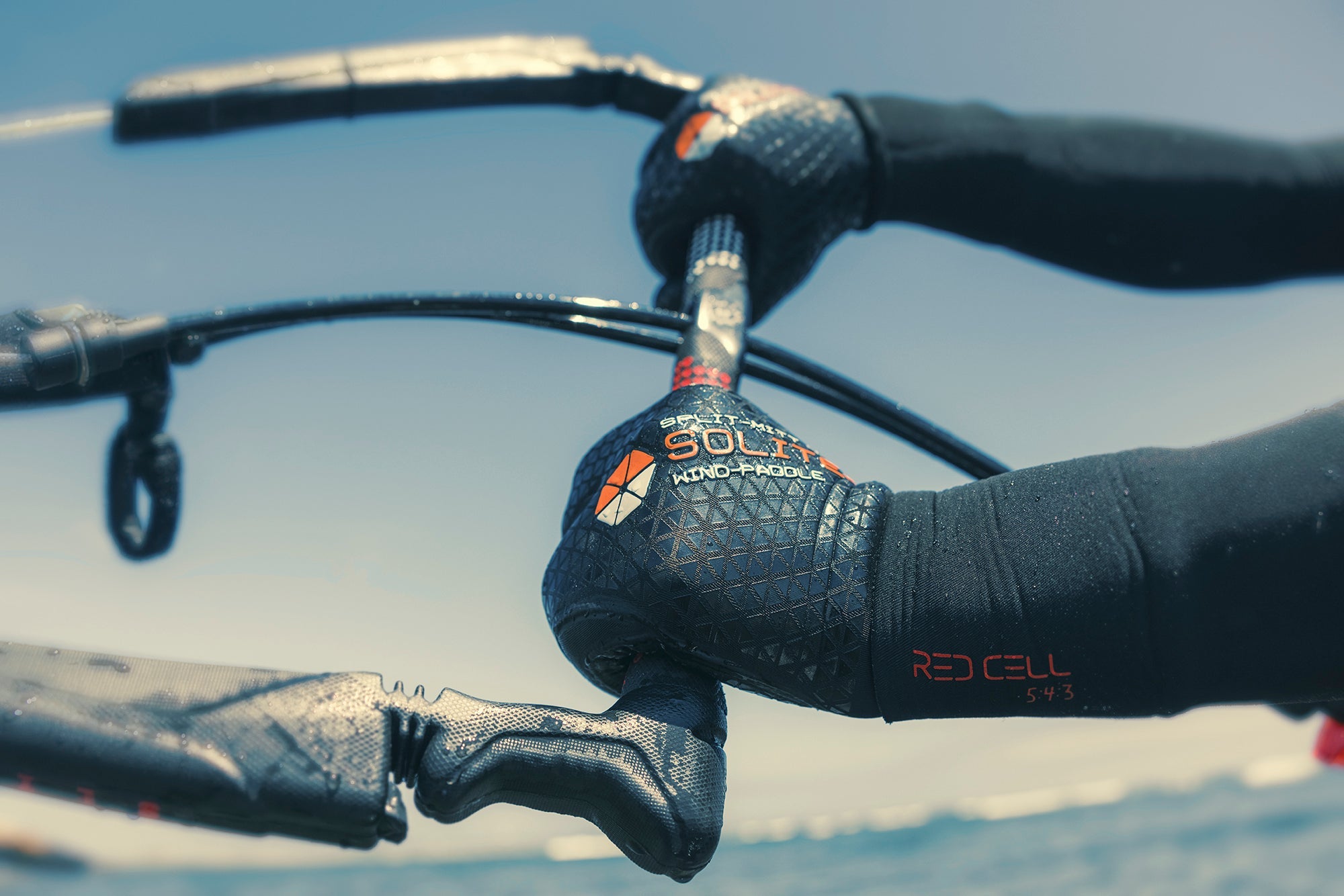 Close-up of hands wearing 4:3 Wind/Paddle Split-Mitt Wetsuit Gloves gripping equipment on the water.