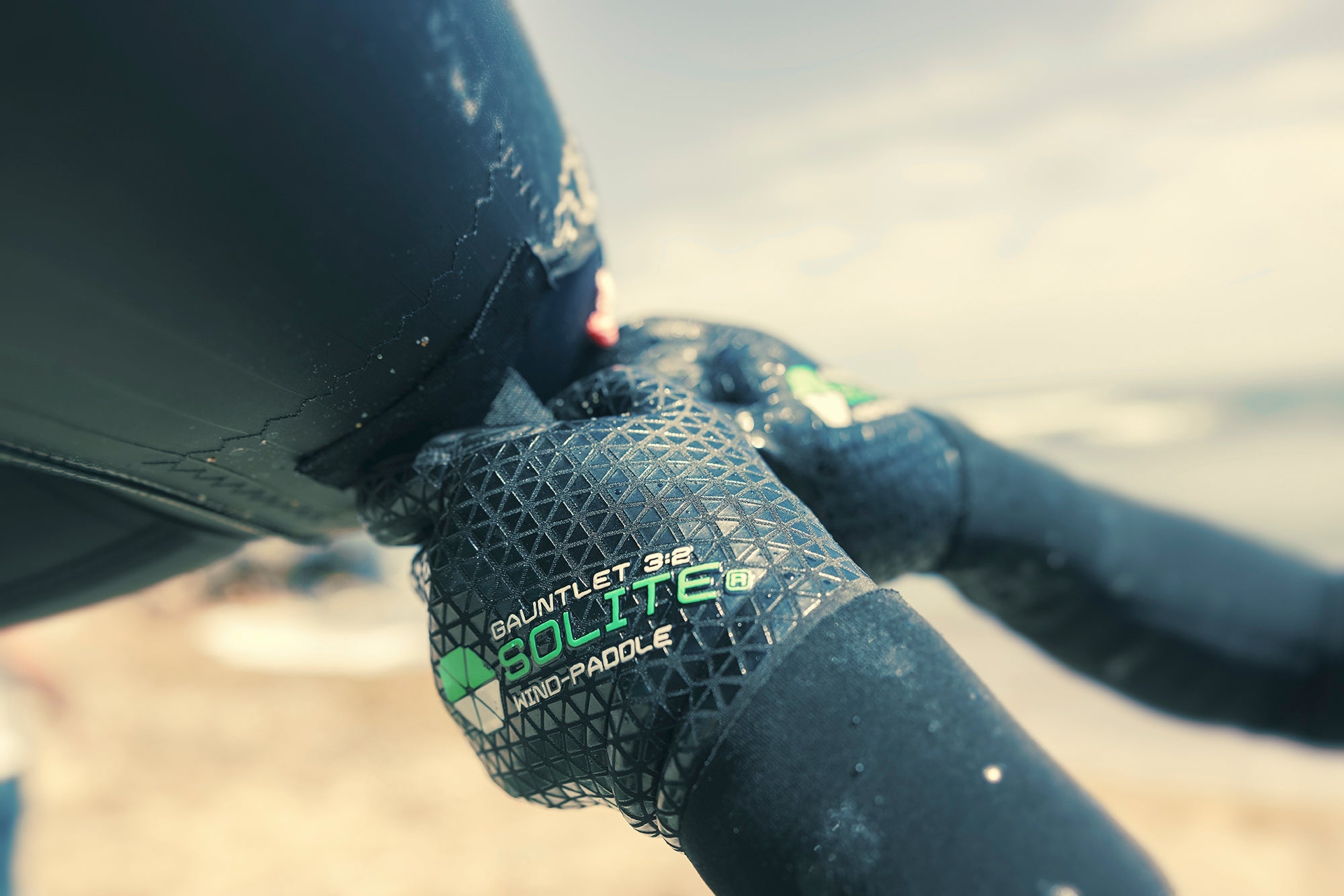 3:2 Wind/Paddle Gauntlet Wetsuit Gloves gripping a surfboard for optimal performance in cold water.