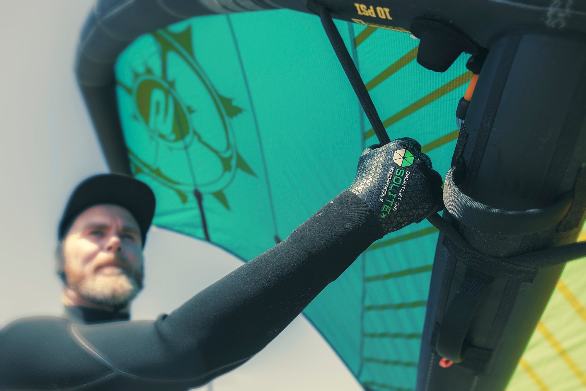 A person wearing 3:2 Wind/Paddle Gauntlet Wetsuit Gloves, gripping a windsurfing sail during a sunny day.