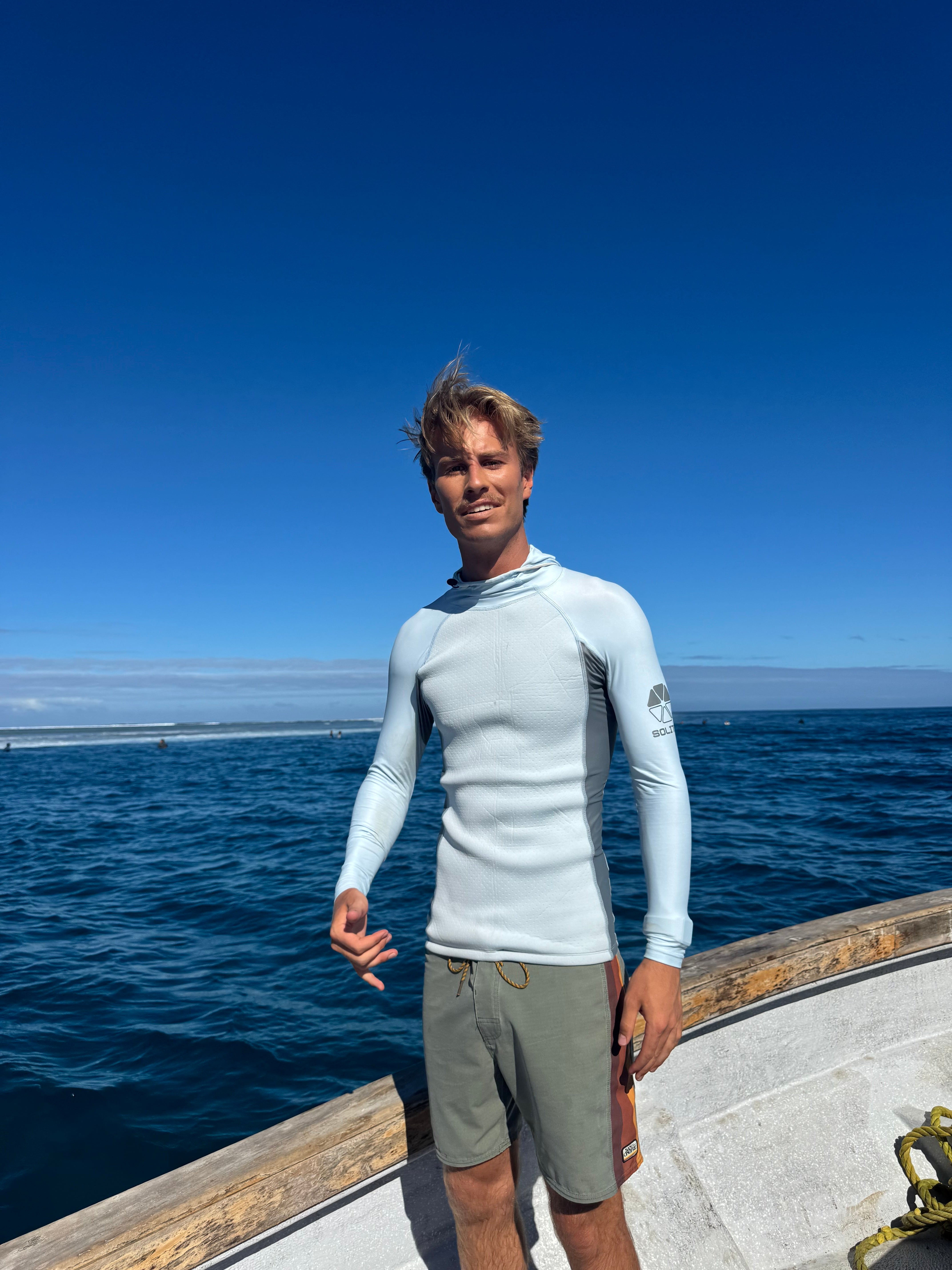 Young man wearing Convertible Neo-Front Rash Guard on a boat by the ocean, showcasing comfort and style.