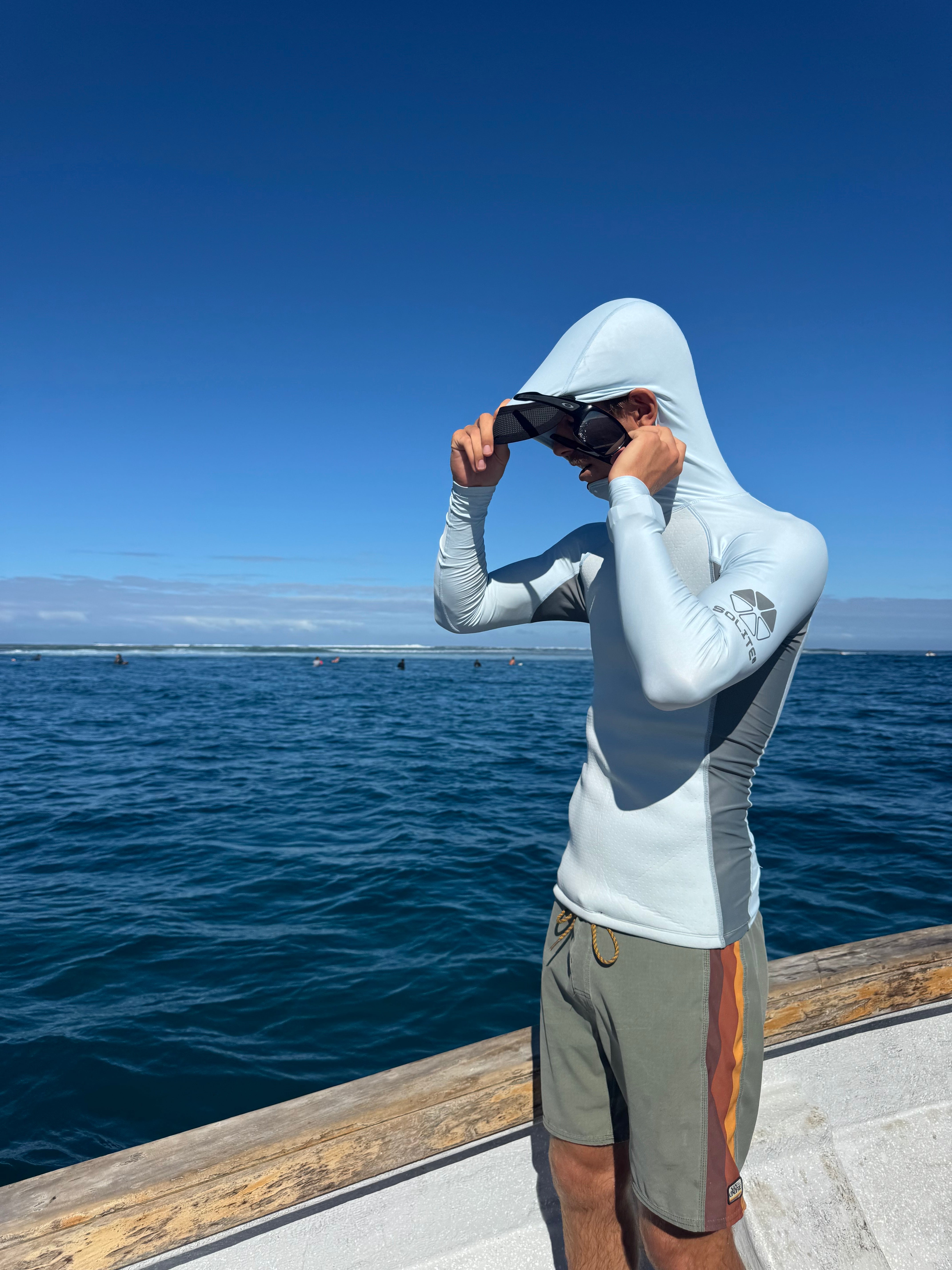 Person wearing a Convertible Neo-Front Rash Guard with a hood, standing on a boat by the water.