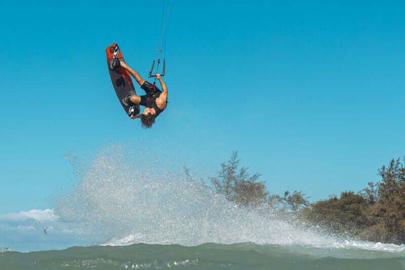 A rider performing a jump on the Ozone Code V5 Kiteboard – Freeride Performance Twintip against a clear blue sky.