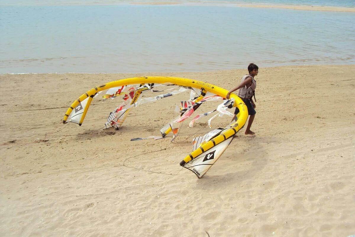 A child pulling a yellow kite from the water's edge, illustrating the joy of kite and wing activities on the beach.