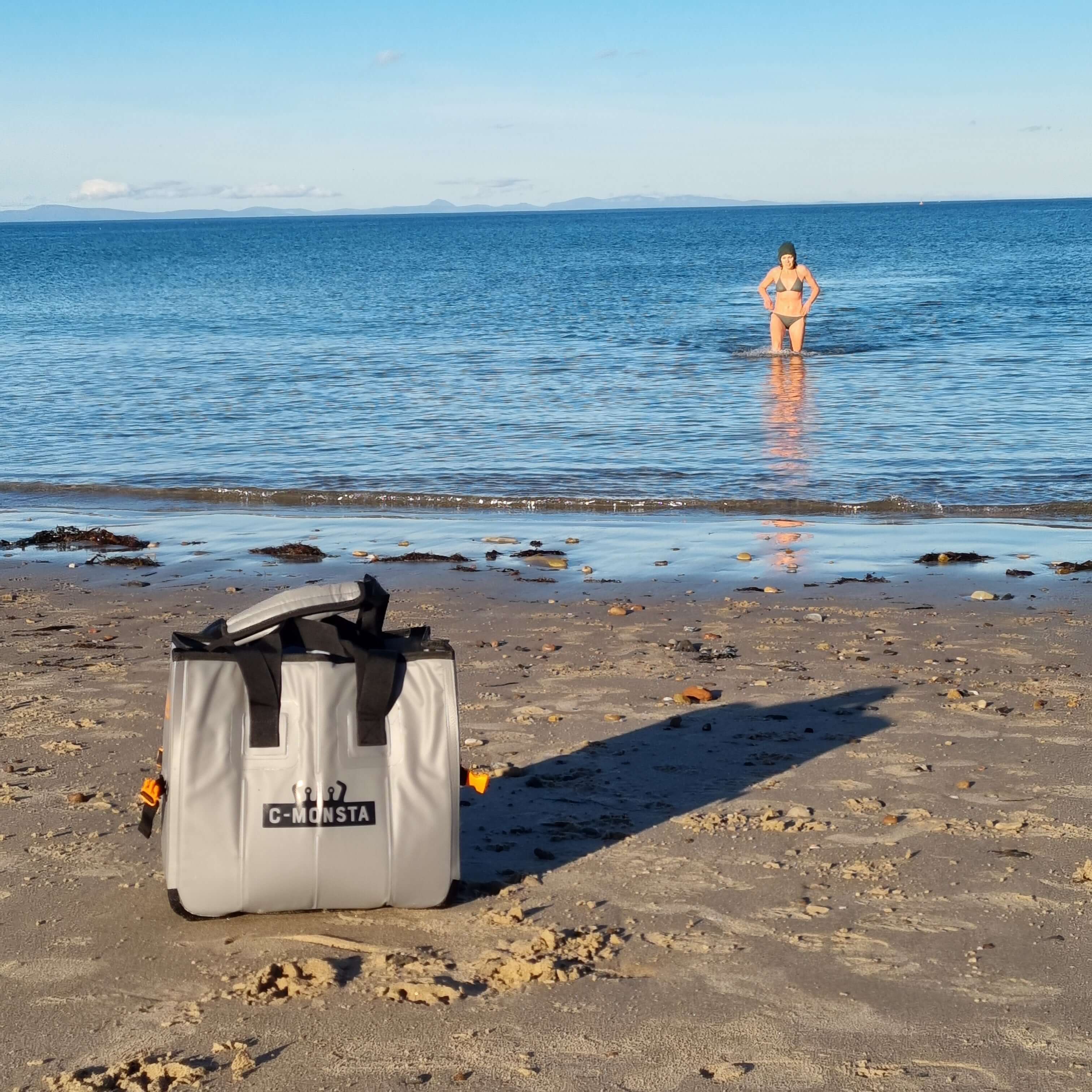 C-Monsta Mini Split Bag | Compact Wet & Dry Gear Bag on the beach with a swimmer in the background.
