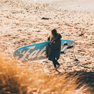 Fatstick AirStick 10'6 Inflatable SUP Package 2026 being carried on a beach by a person in a coat.