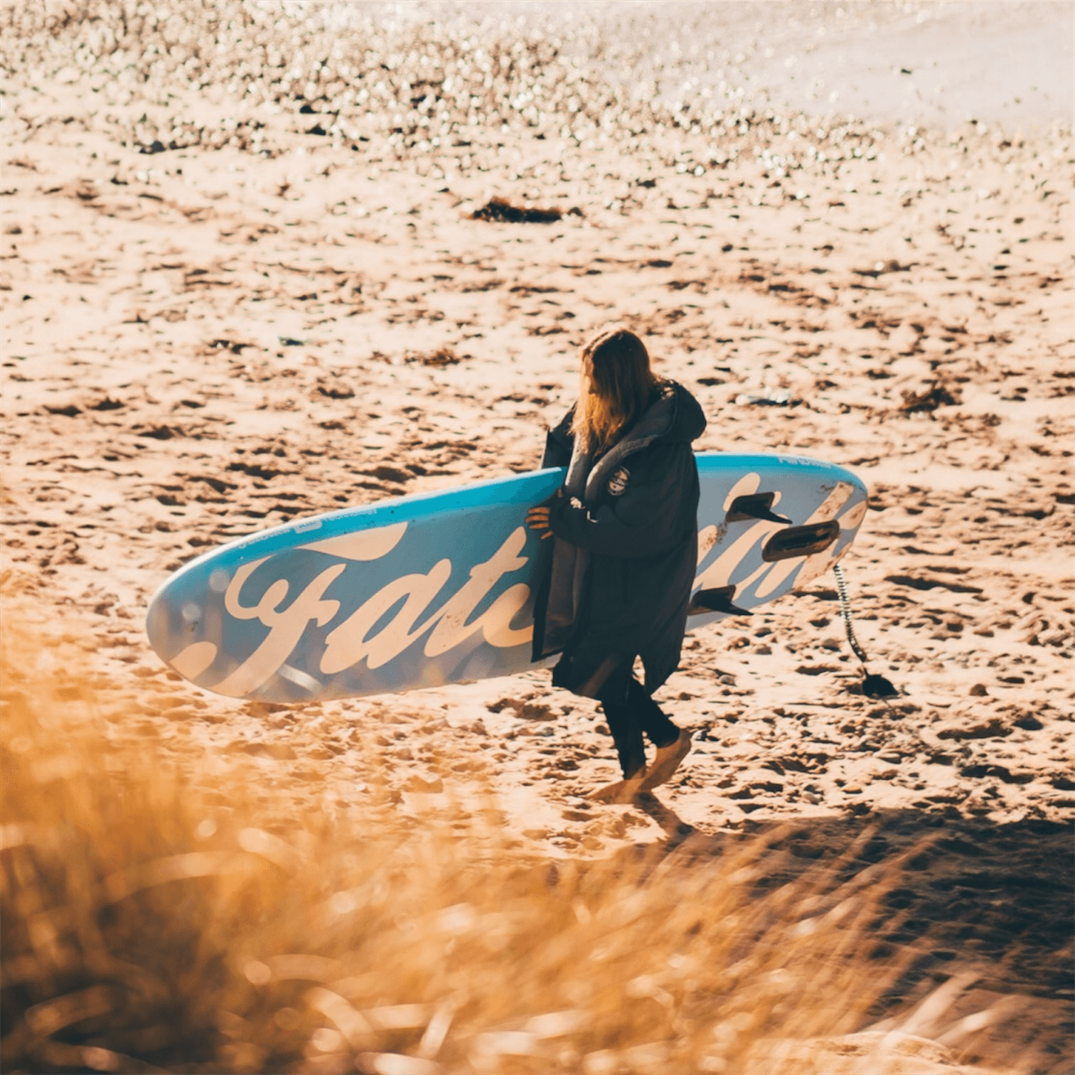 Fatstick AirStick 10'6 Inflatable SUP Package 2026 being carried on a beach by a person in a coat.