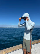 Person wearing a Convertible Neo-Front Rash Guard with a hood, standing on a boat by the water.