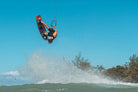 A rider performing a jump on the Ozone Code V5 Kiteboard – Freeride Performance Twintip against a clear blue sky.