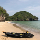 Kaafu Solo Fishing Kayak | Plastic Neutral | Yellow | Complete Package resting on a sandy beach beside a lush green island.